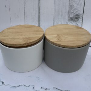 Two ceramic jars with wooden lids on a marble surface.
