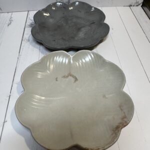 Two ceramic flower-shaped plates, one gray and one white, on a white wooden surface.
