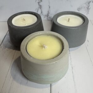 Three handmade candles in concrete holders on a white wooden surface.