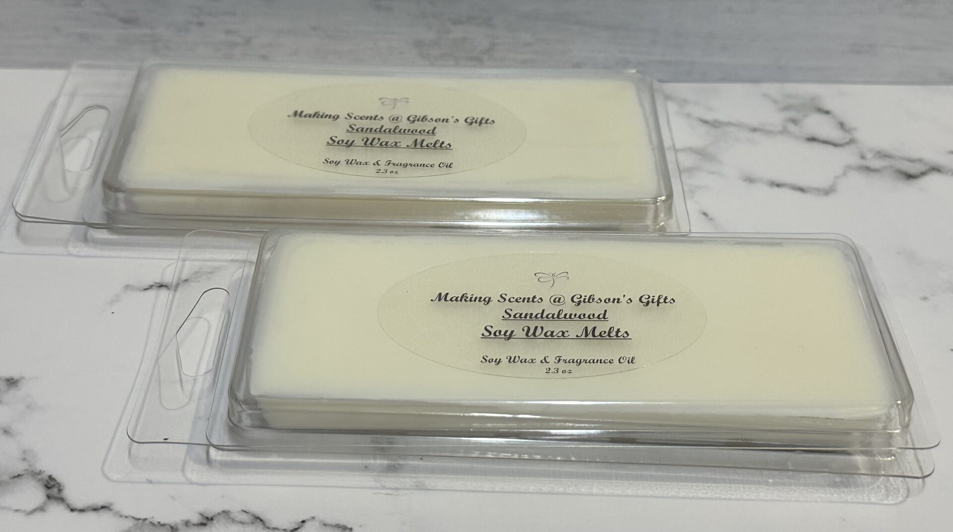 Two bars of handmade soap labeled with natural ingredients on a marble surface.
