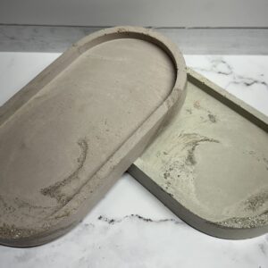 Two minimalist concrete trays with subtle texture on a marble surface.