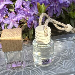 A clear glass perfume bottle with a wooden cap and purple flowers in the background.
