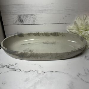 Oval ceramic dish with a rustic, handmade look on a marble surface.