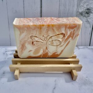 Handmade soap bar with butterfly design on a wooden soap holder.