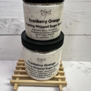 Two jars of Cranberry Orange Whipped Soap stacked on a wooden rack.