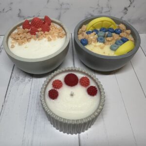 Three creatively decorated dessert bowls with fruit toppings on a wooden surface.