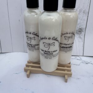 Bottles of handmade lotion with elegant labels on a small wooden stand.